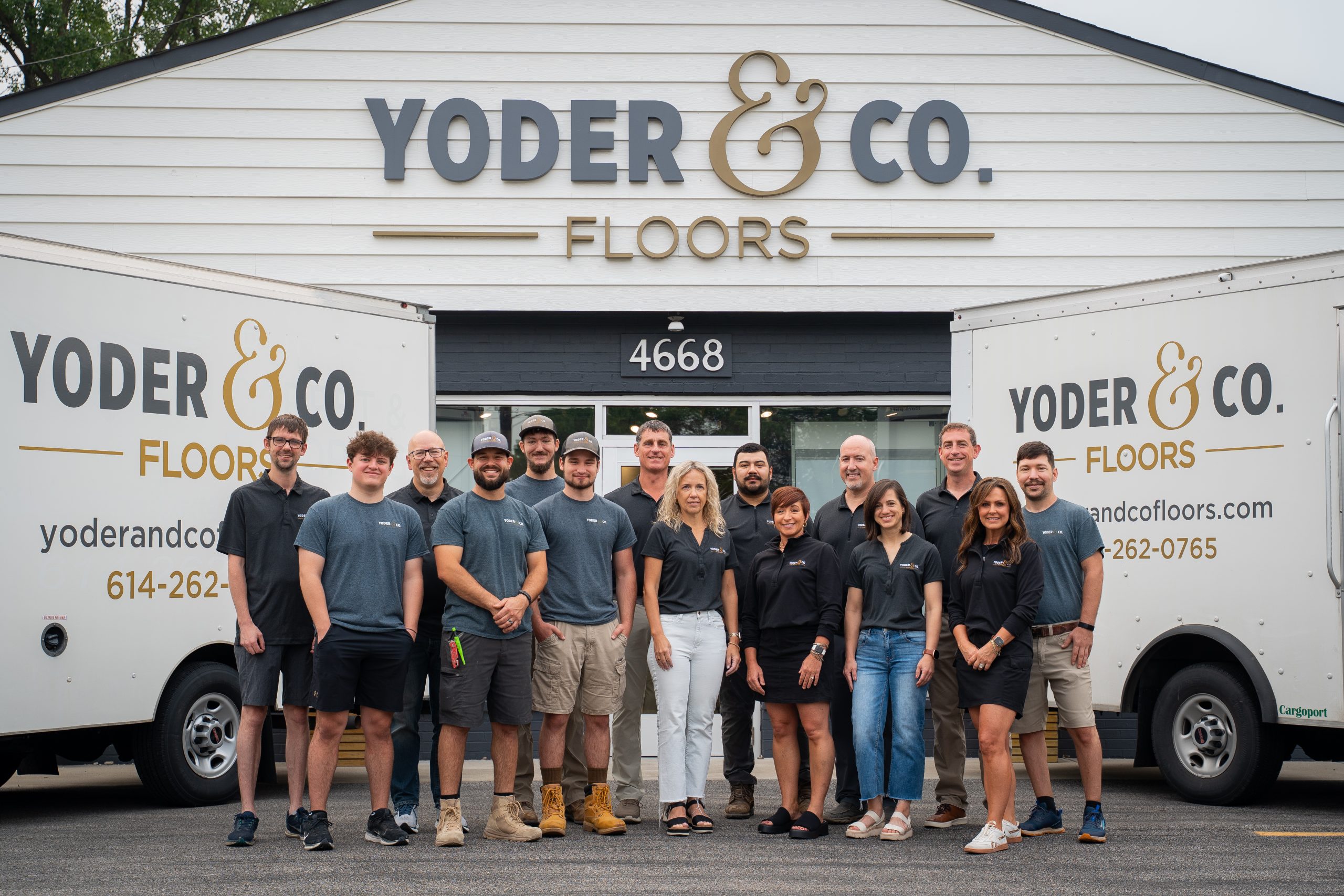 IMG_8907 The Yoder & Co. Floors team standing together in front of their showroom entrance, with two company vans visible on either side
