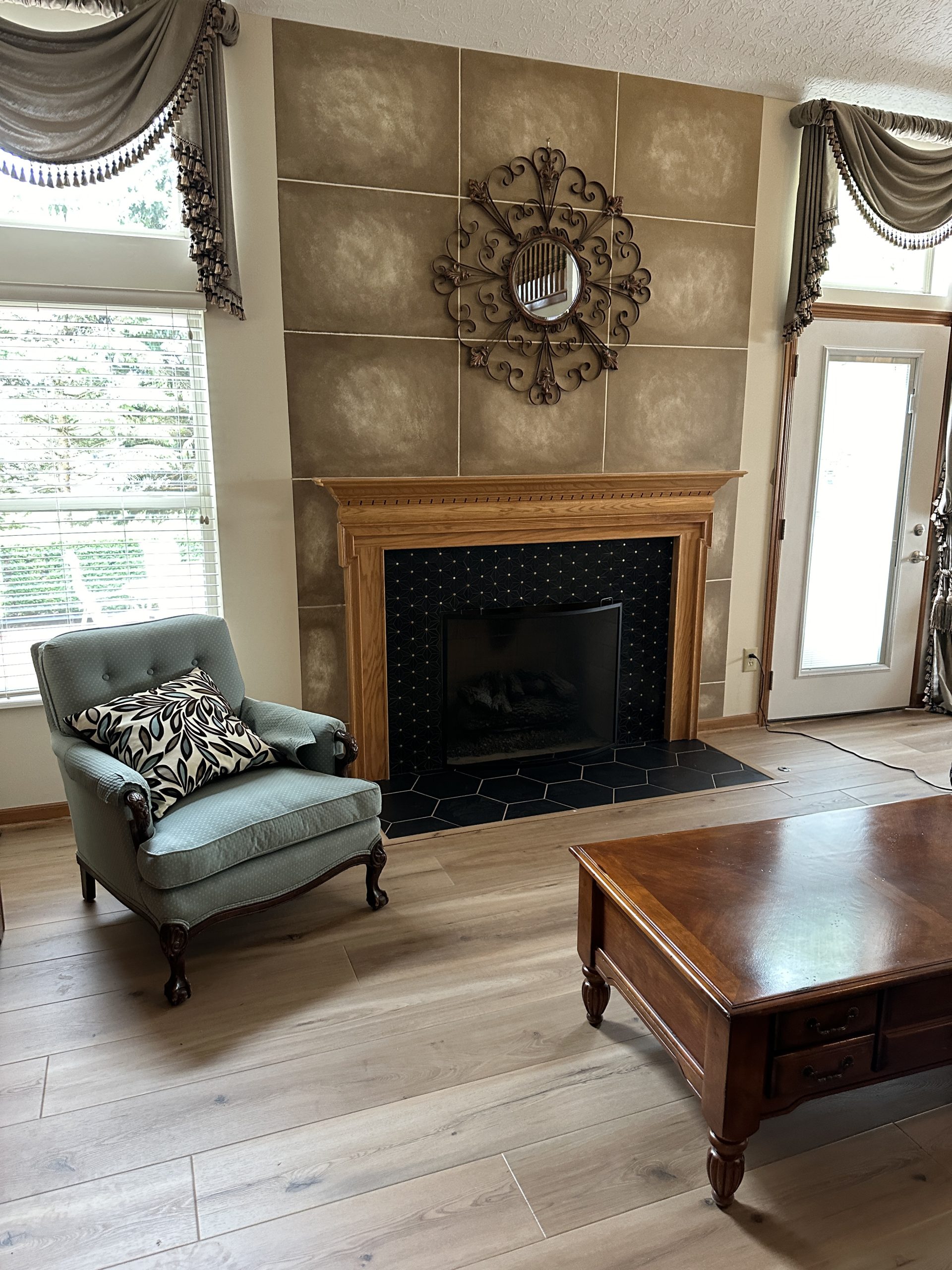 Elegant living room with a tile fireplace and a green upholstered chair on light taupe hardwood floors.
