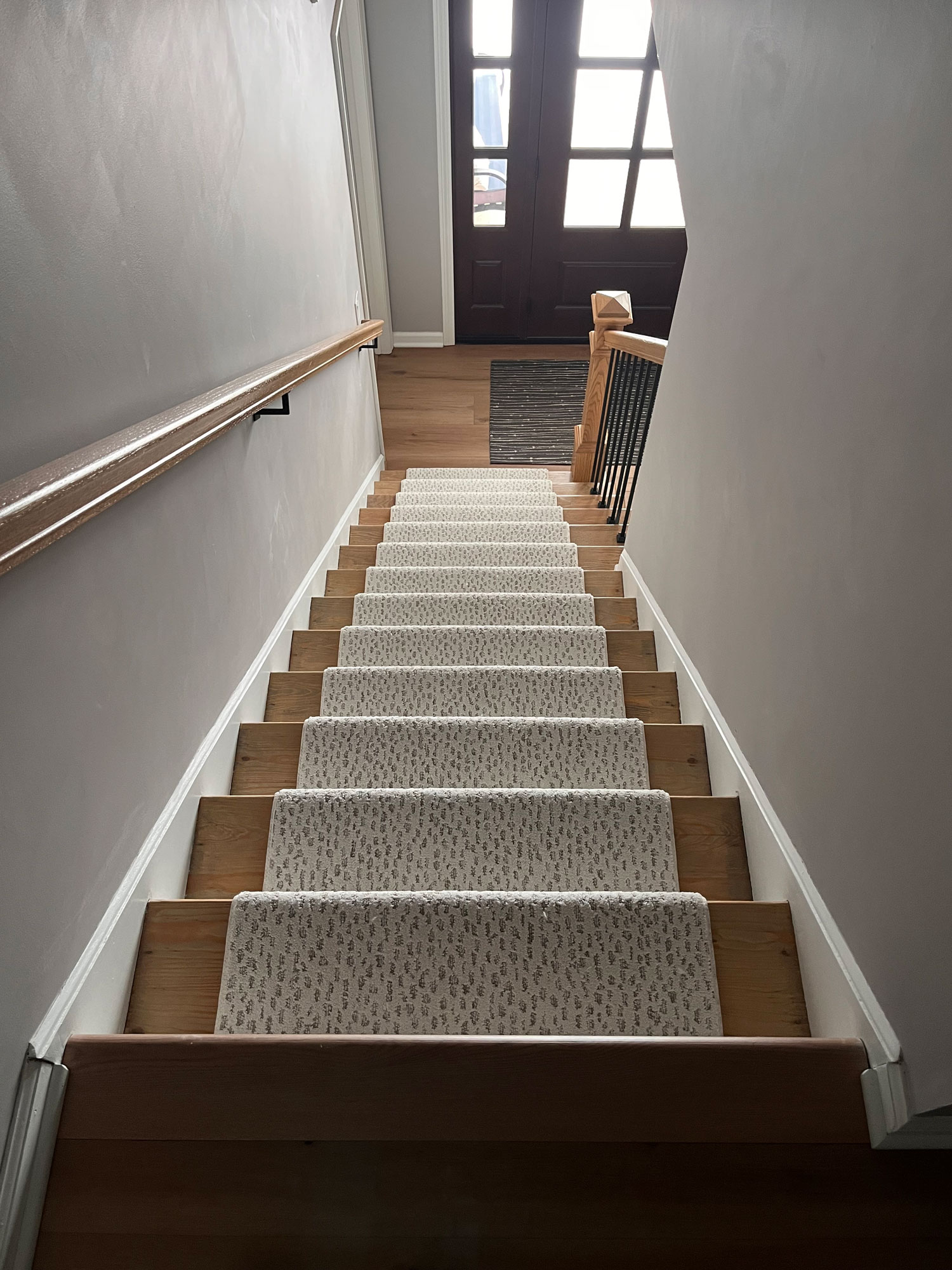 A beige, patterned Anderson Tuftex stair runner from Yoder Floors installed on a set of hardwood floor stairs.