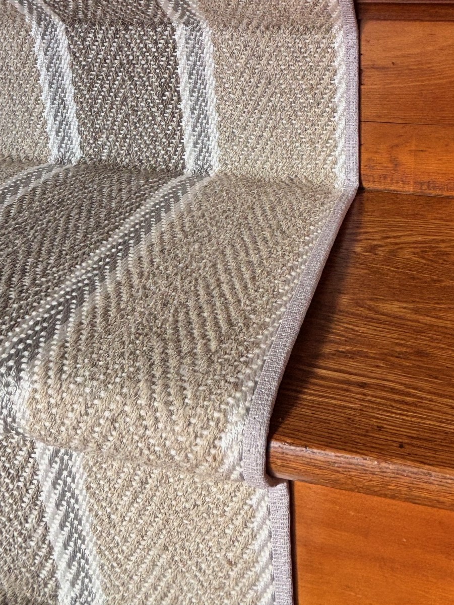A close-up view of a Yoder custom beige area rug corner featuring a navy blue straight binding tape edge, providing a clean and tailored finish.