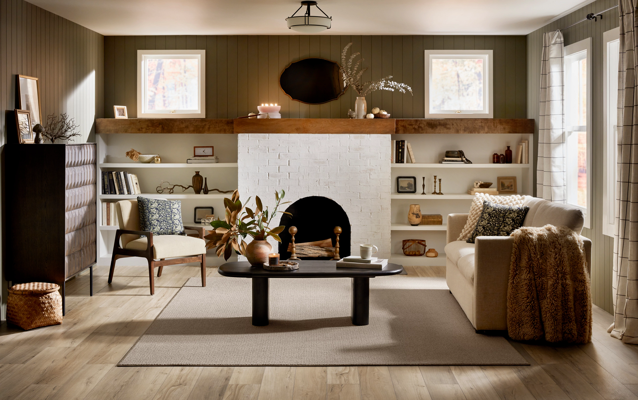 A custom-cut area rug adds warmth and texture over light, wood-look LVP, grounding a living room filled with vintage finds, a painted brick fireplace, and a faux fur throw.